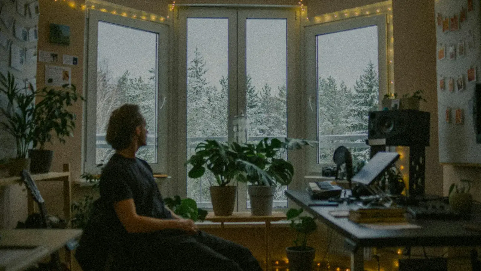 A person sitting in a creative workspace, looking out the window and reflecting beside a music production desk.